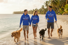 Three people walking along a sandy beach with their dogs, wearing matching royal blue hoodies that read 'My Therapist Barka' in white and orange text.