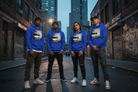 Four people standing on a city street wearing matching bright blue hoodies with a large black-and-white graphic print on the chest.