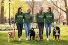 Four women walking dogs on a sunny park lawn, wearing matching green crewneck sweatshirts that read 'My Therapist Bark's' in white and orange text.
