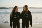 Two people wearing 'Salt Air Beach Hair' sweatshirts on a beach.